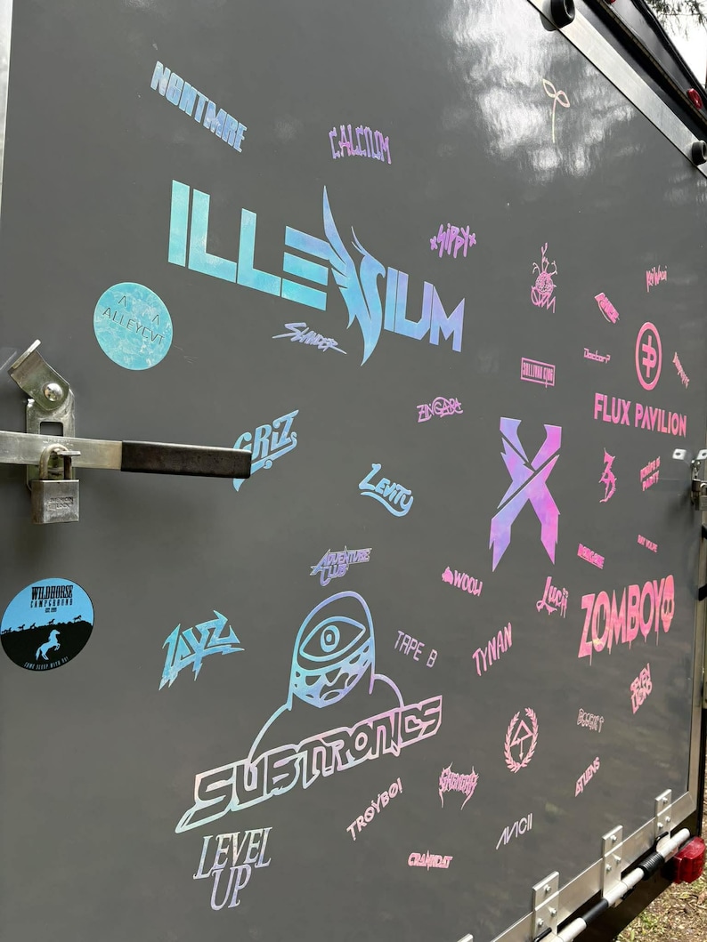 K&ouml;nnte beinhalten: Eine graue Anh&auml;ngert&uuml;r, die mit holografischen Aufklebern bedeckt ist. Die Aufkleber zeigen verschiedene Logos und Texte, darunter "ILLENIUM", "SUBTRONICS" und "ZOMBOY". Andere Aufkleber zeigen Namen und Symbole.