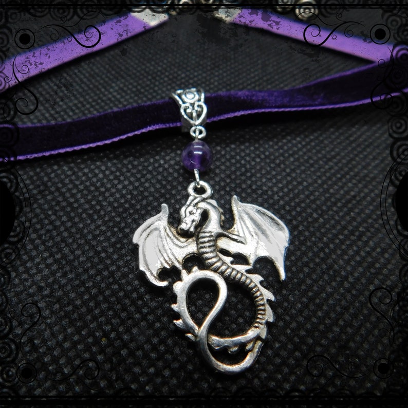 May include: A silver dragon pendant necklace with a purple velvet choker. The dragon is detailed with wings and a curled tail. A purple amethyst bead hangs above the dragon.