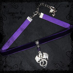 May include: Purple velvet choker necklace with a silver dragon pendant and a purple gemstone. The necklace is accented with a purple ribbon and a silver chain.