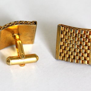 May include: A pair of gold cufflinks with a textured, chain-link design. One cufflink has a traditional back closure, while the other has a more modern, square design.