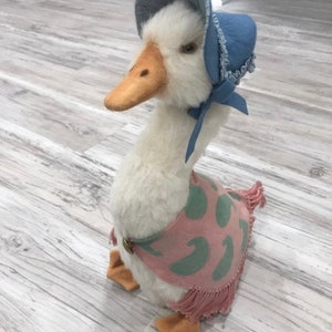 Może przedstawiać: Biała pluszowa gęś w niebieskim czepeczku i różowym szalu z zielonym wzorem paisley. Gęś ma żółty dziób i pomarańczowe łapy.