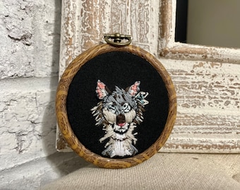 May include: Embroidered wolf portrait in a brown wooden hoop with a black fabric background.