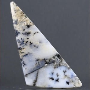 May include: A triangular shaped, white agate cabochon with black dendritic inclusions. The agate has a translucent appearance with a white, gray, and black color scheme.