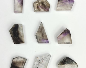 May include: Nine polished gemstone slices in various geometric shapes. The stones feature a mix of clear, purple, and brown hues. Each stone has a unique pattern and shape, with some resembling trapezoids and others more abstract forms.