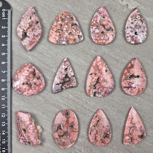 Natural ocean jasper cabochons with pink and coral orbicular patterns and natural druzy pockets arranged on a neutral stone background, each piece uniquely shaped.