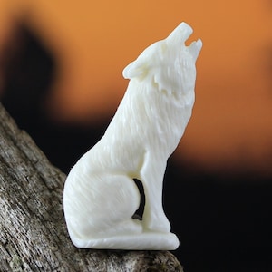 Könnte beinhalten: Eine geschnitzte, weiße Wolfsfigur in einer heulenden Pose. Der Wolf sitzt mit erhobenem Kopf und offenem Maul. Die Figur hat eine detaillierte Fellstruktur. Der Hintergrund ist verschwommen.