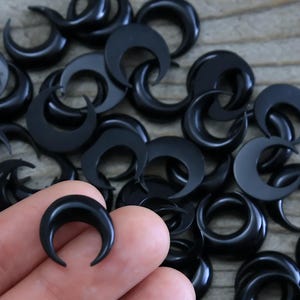 Könnte beinhalten: Ein Haufen schwarzer Halbmond-Ohrringe. Die Ohrringe sind aus einem glatten, polierten Material gefertigt.