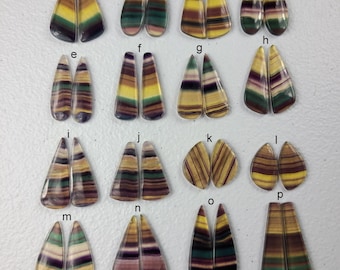 Puede incluir: Conjunto de 16 pares de cabujones de fluorita arcoíris iridiscente, cada par está etiquetado con una letra de la a a la p. Los cabujones tienen forma de lágrima y presentan una variedad de colores, incluyendo morado, verde, amarillo y marrón.