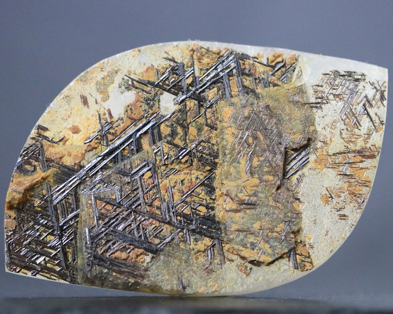 Large, freeform polished cabochon of Sagenite Rutilated Quartz with a light matrix and striking black and reddish-brown rutile needle inclusions forming intricate, geometric patterns.