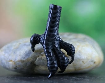Puede incluir: Un colgante de garra de pájaro negro y detallado. La garra está hecha de un material negro liso y tiene una superficie texturizada. La garra es un diseño popular para joyas y a menudo se usa para representar fuerza y poder.