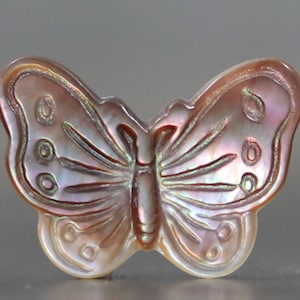 May include: A pink iridescent mother of pearl butterfly charm with intricate details. The butterfly has a delicate, carved design and a pearlescent finish.