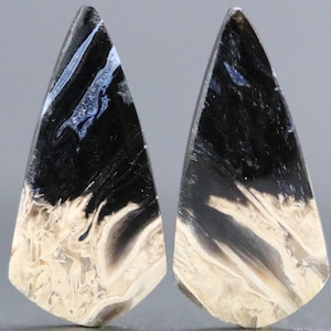 Könnte beinhalten: Paar schwarze, weiße und blaue Achat-Cabochons in Tropfenform. Die Cabochons haben ein wirbelndes Muster aus Schwarz, Weiß und Blau.