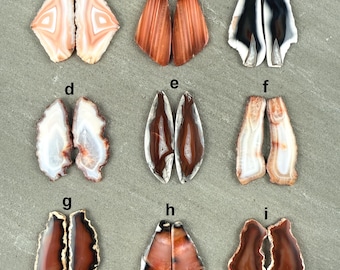 May include: Nine pairs of polished agate stones in various shapes and colors, including white, brown, orange, and black. The stones are displayed on a gray surface, showcasing their natural patterns and textures. These stones are ideal for jewelry making.