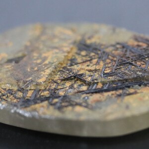 May include: A close-up of a clear quartz crystal with a unique pattern of black and brown inclusions. The crystal is smooth and polished, with a slightly rounded shape.