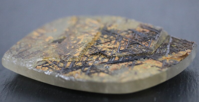 May include: A close-up of a clear quartz crystal with a unique pattern of black and brown inclusions. The crystal is smooth and polished, with a slightly rounded shape.