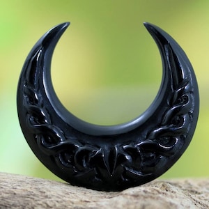 Op de afbeelding: Zwarte halve maanvormige oorplug met een ingewikkeld gesneden ontwerp.