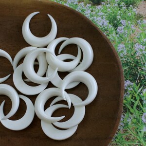 May include: A collection of white crescent moon shaped earrings, displayed on a wooden surface.