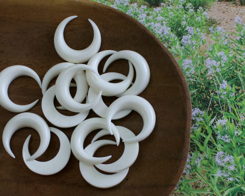 May include: A collection of white crescent moon shaped earrings, displayed on a wooden surface.