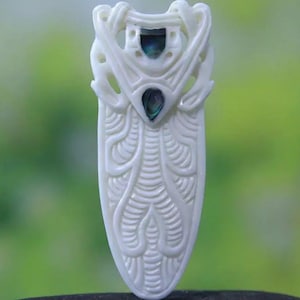 Tall white carved bone pendant with two abalone shell inlays, approx. 62mm long.