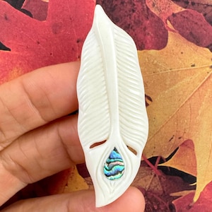 White hand-carved buffalo bone pendant in the shape of a feather with an iridescent abalone shell inlay at the base.