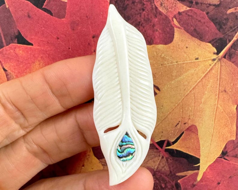 White hand-carved buffalo bone pendant in the shape of a feather with an iridescent abalone shell inlay at the base.