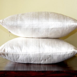 May include: Two white silk pillow covers stacked on top of each other. The pillow covers are made of a soft, luxurious fabric with a subtle sheen.