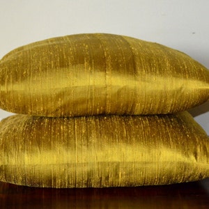 May include: Two gold-coloured throw pillows made of a textured fabric. The pillows are stacked on top of each other.