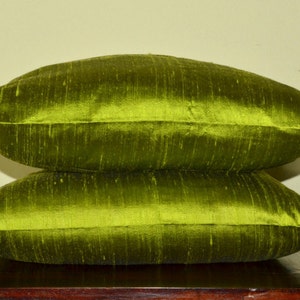 May include: Two green silk pillow covers stacked on top of each other. The pillow covers are a deep green colour and have a subtle sheen.
