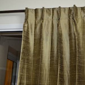 May include: A set of gold-colored curtain rods with finials, holding a pair of pleated, olive green curtains.