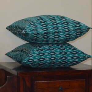 May include: Two teal blue and white patterned throw pillows stacked on top of each other on a dark wood table.