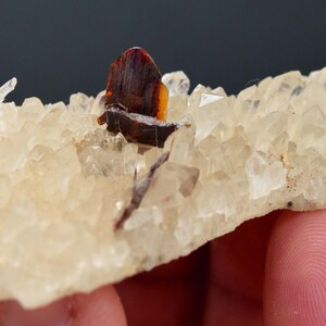 May include: A cluster of quartz crystals with a dark brown and orange mineral formation. The quartz crystals are clear and have a slightly yellow tint. The mineral formation is a dark brown color with orange and yellow accents.