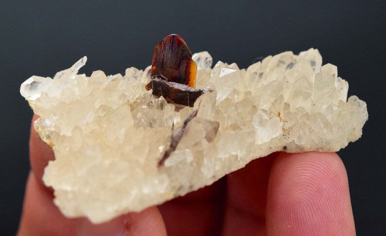 May include: A cluster of quartz crystals with a dark brown and orange mineral formation. The quartz crystals are clear and have a slightly yellow tint. The mineral formation is a dark brown color with orange and yellow accents.