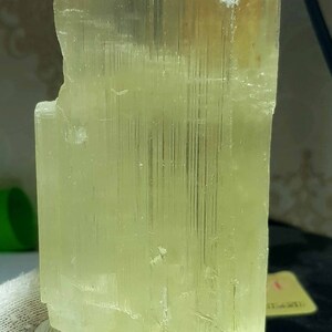 May include: A translucent, pale yellow crystal formation. The crystal has a rectangular shape with a rough, textured surface and visible internal striations. The overall color is a soft, light yellow.