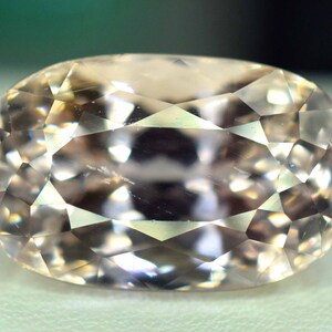 Puede incluir: Una gema facetada de forma ovalada con un tono melocot&oacute;n p&aacute;lido. La superficie de la gema est&aacute; dividida en numerosas facetas triangulares peque&ntilde;as, creando un efecto brillante. La piedra se encuentra sobre un fondo suave y neutro.
