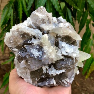 以下が含まれることがあります： 立方晶と結晶構造が複雑に組み合わされた、大きな天然鉱物標本。標本は、濃いグレー、白、透明な結晶構造が混ざり合い、表面はざらざき、質感があります。 全体的な形状は不規則で有機的です。
