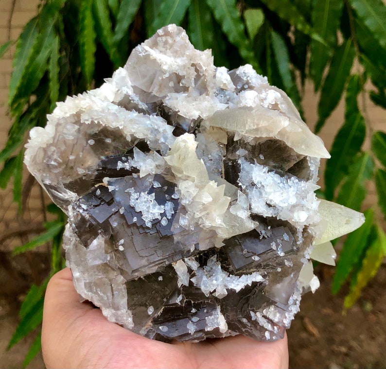 以下が含まれることがあります： 立方晶と結晶構造が複雑に組み合わされた、大きな天然鉱物標本。標本は、濃いグレー、白、透明な結晶構造が混ざり合い、表面はざらざき、質感があります。 全体的な形状は不規則で有機的です。