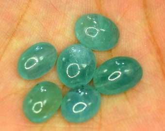 May include: Six oval-shaped, translucent gemstones in varying shades of teal and aqua. The polished stones have a smooth, glossy surface, reflecting light. The gemstones are displayed against a warm, skin-toned background.