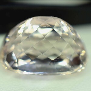 Puede incluir: Una gema facetada de color melocot&oacute;n claro, con una parte superior redondeada. La superficie est&aacute; tallada con numerosas facetas peque&ntilde;as en forma de diamante, creando un efecto brillante. La gema se encuentra sobre un fondo suave y neutro.