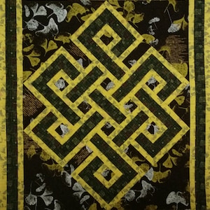 May include: A yellow and green geometric pattern in the shape of a knot, on a dark brown background with white leaf designs.