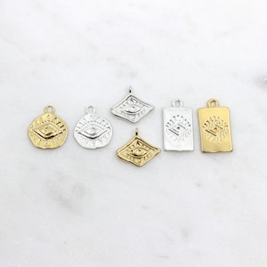 May include: Six gold and silver charms featuring an eye design. The charms are in different shapes, including round, square, and diamond.