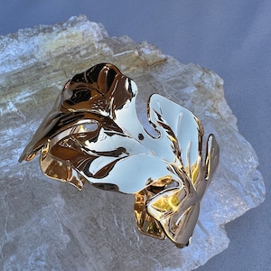 May include: A gold-toned leaf-shaped cuff bracelet. The bracelet is made of metal and has a smooth, polished finish.