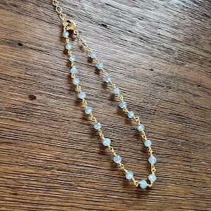 May include: A delicate gold chain bracelet with light blue beads. The bracelet has a lobster clasp closure.