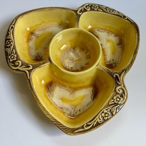 May include: A vintage yellow ceramic serving dish with three triangular compartments and a central round bowl. The dish has a brown floral border and a glossy finish. The interior of the dish has a unique brown and white pattern.
