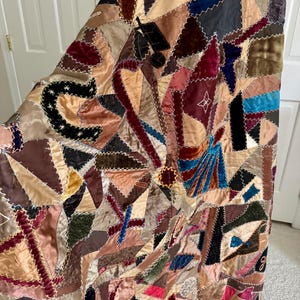 May include: A patchwork quilt with a variety of fabrics in shades of brown, tan, burgundy, and blue. The quilt is made of many small, irregularly shaped pieces sewn together with white stitching. The quilt has a vintage, handcrafted appearance.