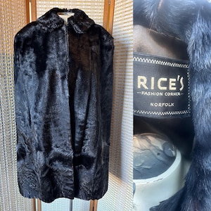 May include: A vintage black fur coat with a wide collar. The coat has a luxurious, textured appearance. The label reads "RICE'S - FASHION CORNER - NORFOLK". The coat is displayed on a wooden hanger against a neutral backdrop.