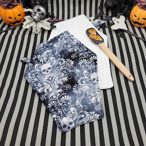 Könnte beinhalten: Zwei Topflappen mit schwarzem und weißem Muster und einem Totenkopfdesign. Ein Topflappen ist weiß mit schwarzem Rand und der andere ist schwarz mit einem weißen Totenkopf und einem floralen Muster.