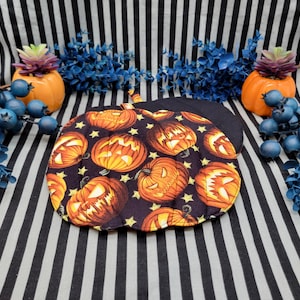 May include: A pair of black and orange pumpkin-themed pot holders with a black background and yellow stars. The pot holders are quilted and feature a pattern of orange jack-o'-lantern faces.