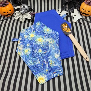 May include: Two blue and white coffin-shaped pot holders with a starry night design. One pot holder is solid blue and the other has a print of Van Gogh's Starry Night. A wooden spatula with a pumpkin face design is included.