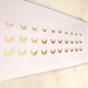 May include: A sheet of gold-colored crescent moon stickers. The stickers are arranged in rows, with each row containing a different size of moon.