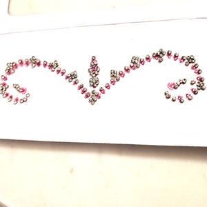 May include: A sheet of clear adhesive backed rhinestones with pink and silver accents. The rhinestones are arranged in a decorative pattern.